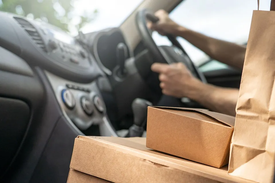Close-up of cardboard food delivery boxes and bags on car seat next to driver.